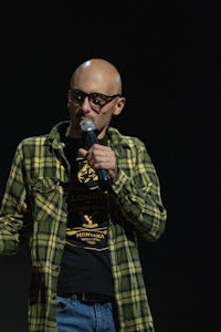 a bald man in a plaid shirt holding a microphone